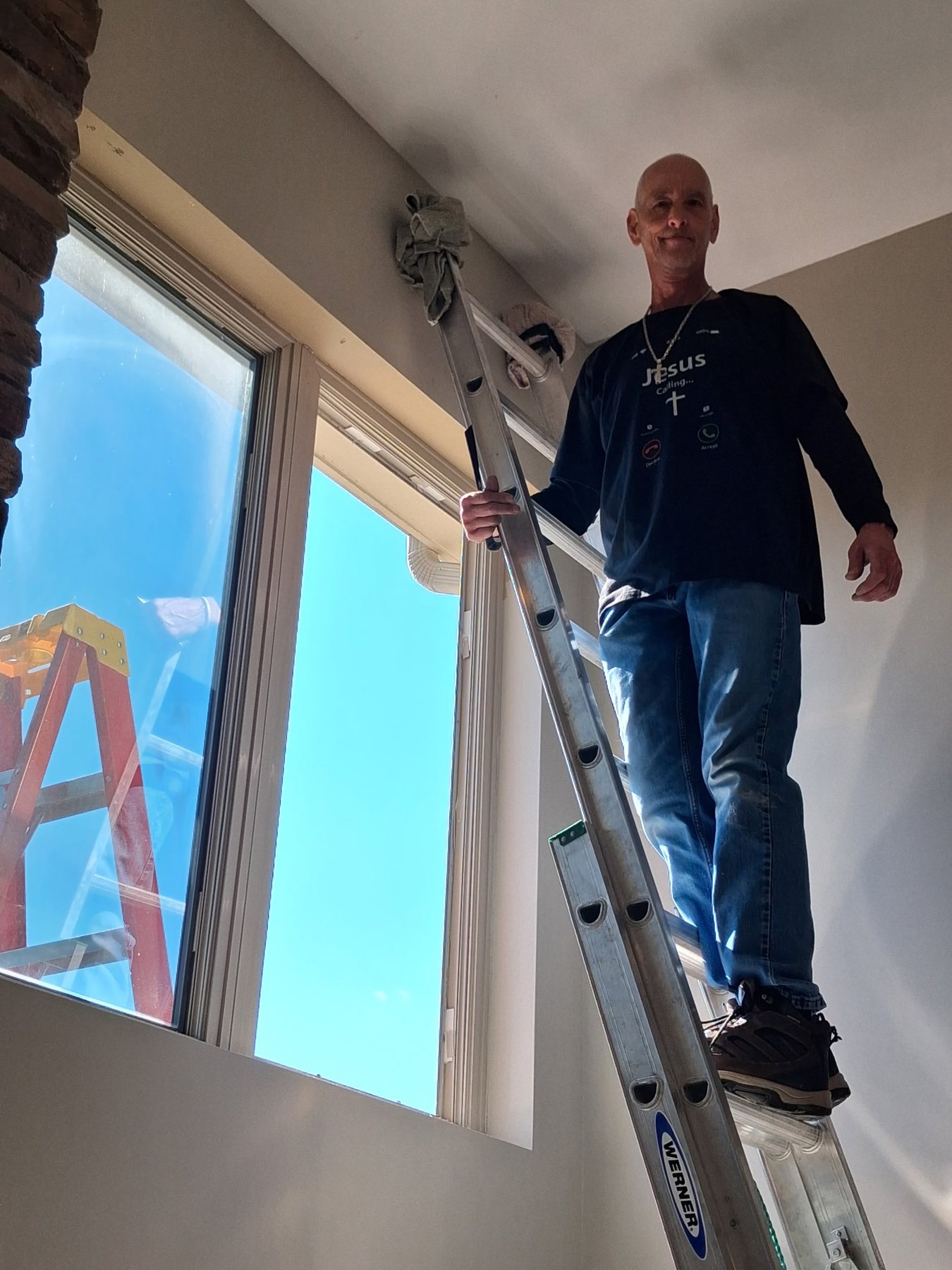 Charles installing a large replacement window pane from a ladder