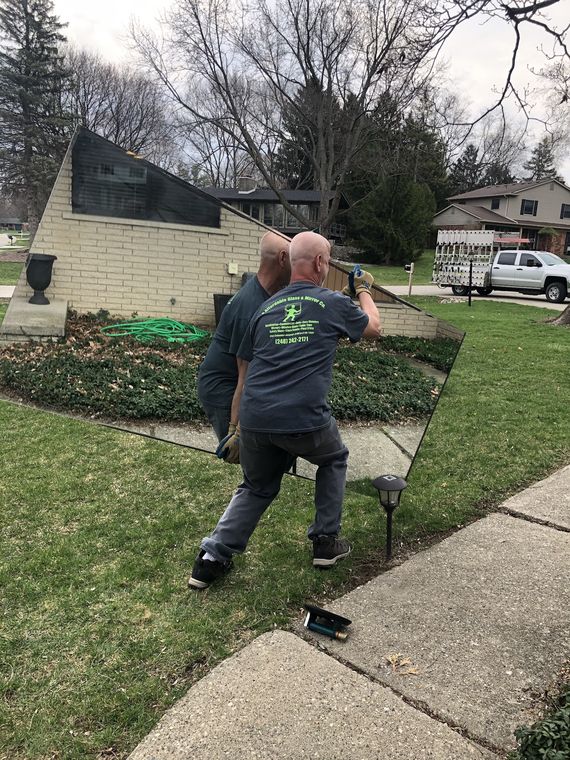 Charles carrying a large mirror across a front lawn