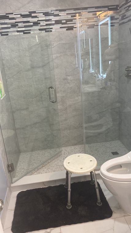 Glass shower enclosure with mosaic tile and a bench